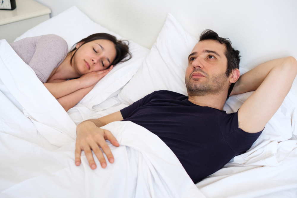 man awake lying in bed with woman 